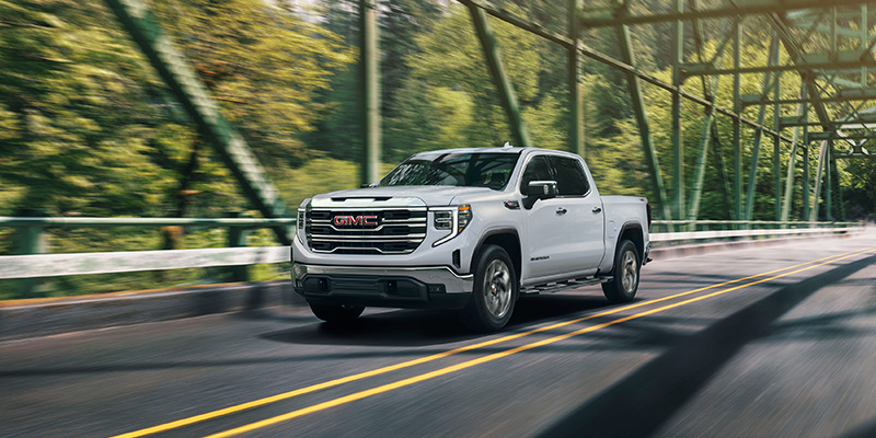 2026 GMC Sierra 1500 crossing a bridge on a green countryside road.
